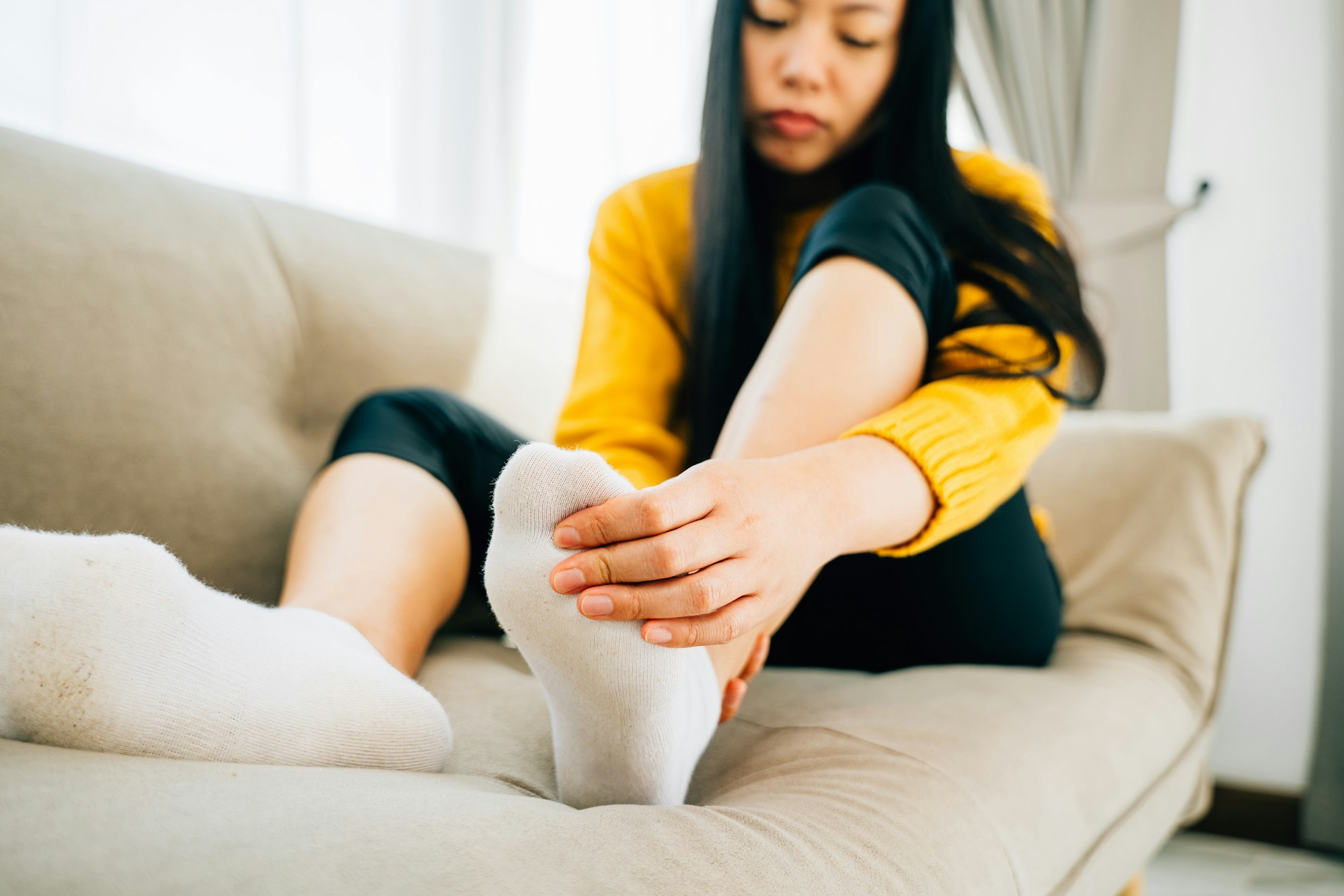 A woman on a sofa massages her painful foot emphasizing the highlighted pain area