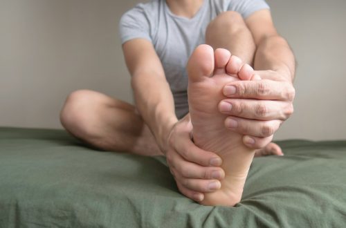 Person massaging their foot due to pain in the sole, arch and toes. Space for text on the left.